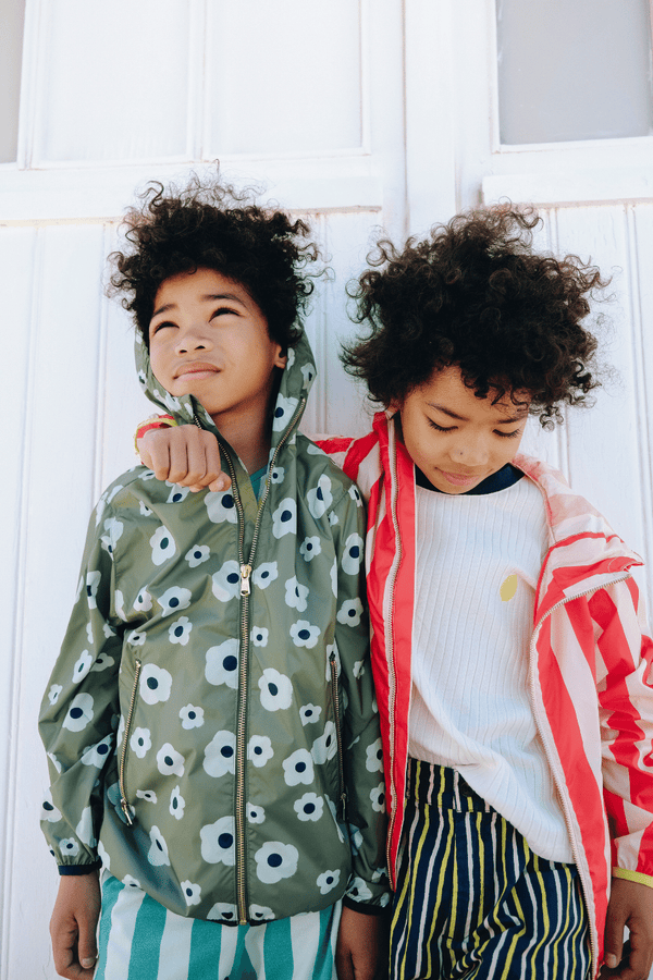 Deux enfant portant le coupe-vent REMY à motif grandes fleurs vertes et le short KIM à rayures vertes, ainsi que le coupe-vent REMY à rayures rouges, vêtements en coton bio certifié GOTS style vintage mixte unisexe