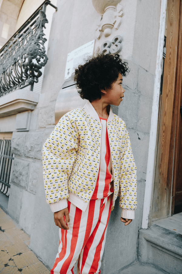 Un enfant porte le débardeur marcel à rayures rouges et le bomber gaby imprimé petites fleurs jaunes, vêtements en coton bio certifié GOTS style vintage