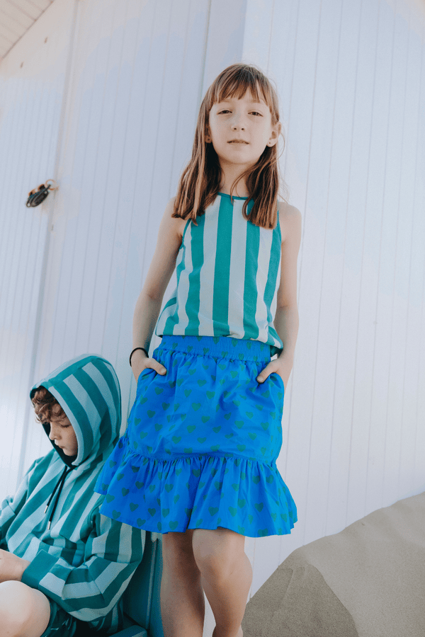 Fille portant le débardeur MARCEL à rayures vertes et le jupe IRMa avec poches et short intégré couleur bleu et imprimé cœurs verts, vêtements en coton bio certifié GOTS style vintage mixte unisexe