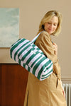 Jeune femme portant le sac weekend stripes, rayé vert et violet. Sac de voyage en coton bio, porté sur l'épaule ou à la main.